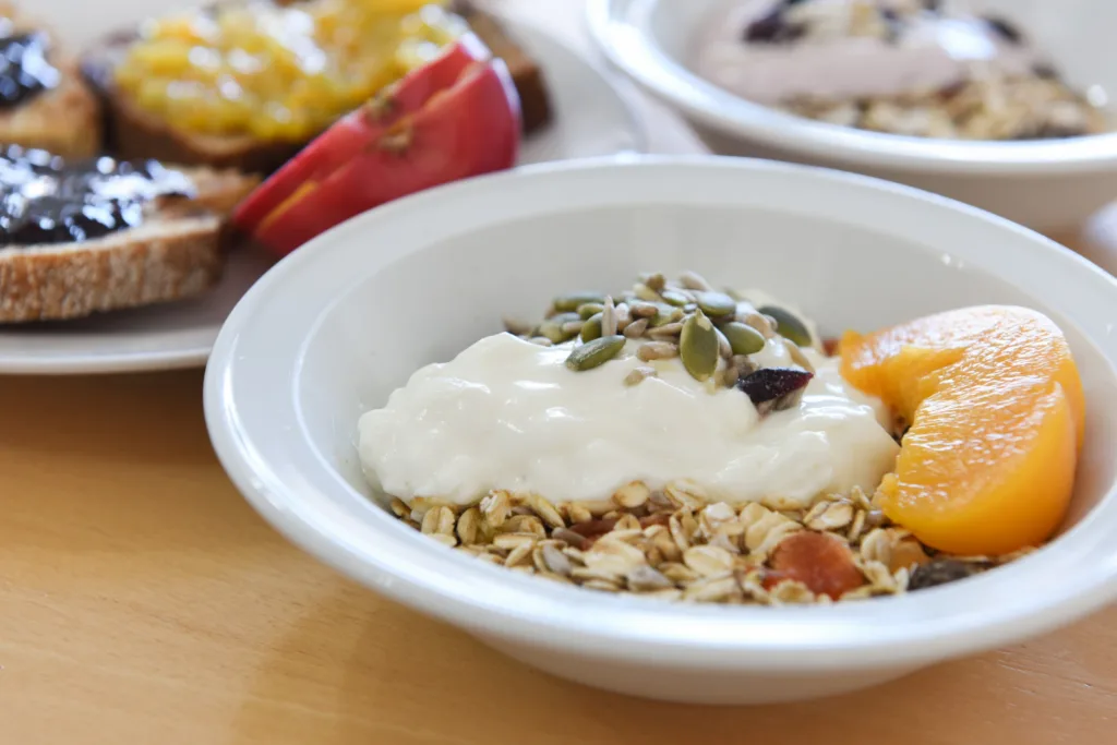 Muesli bowl with yoghurt and peach in front of toast and fruit