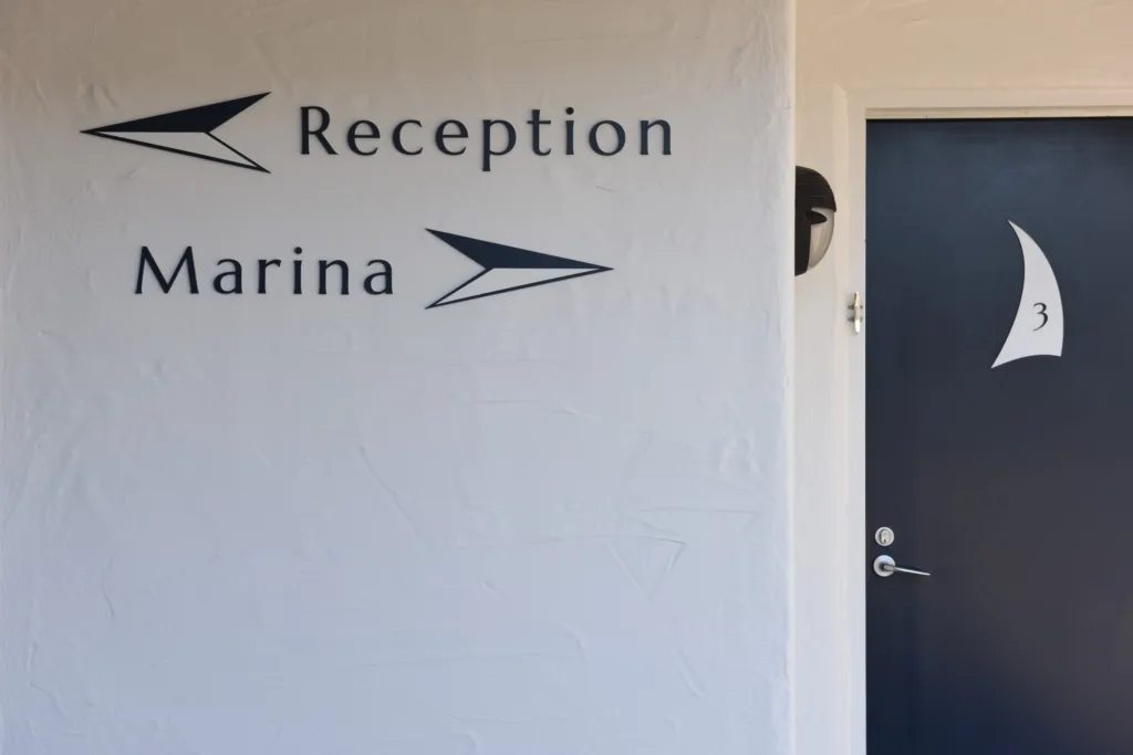 Wall signage pointing to reception and the marina beside a navy room door