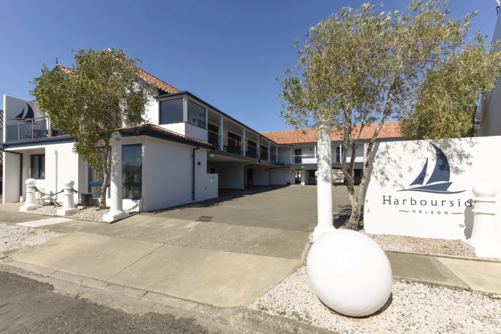 Harbourside Nelson entrance with sail logo sign, white bollards and olive trees