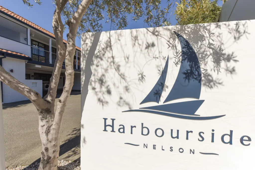 Harbourside Nelson sail logo sign at the entrance under an olive tree